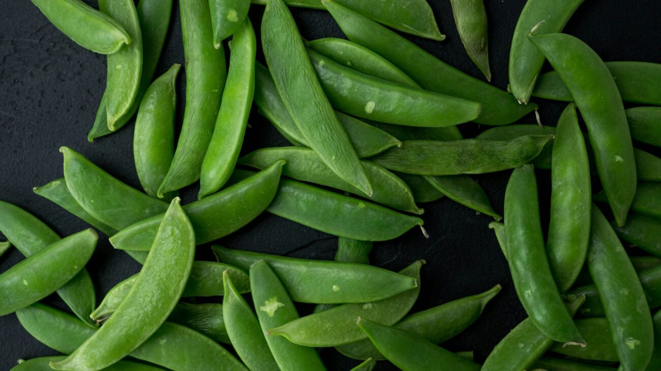 Fresh sugar snap pea pods scattered on a dark slate surface