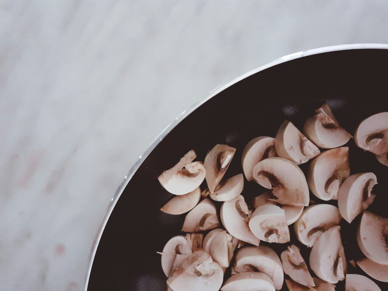 Sliced white button mushrooms in a dark pan on a marble counter
