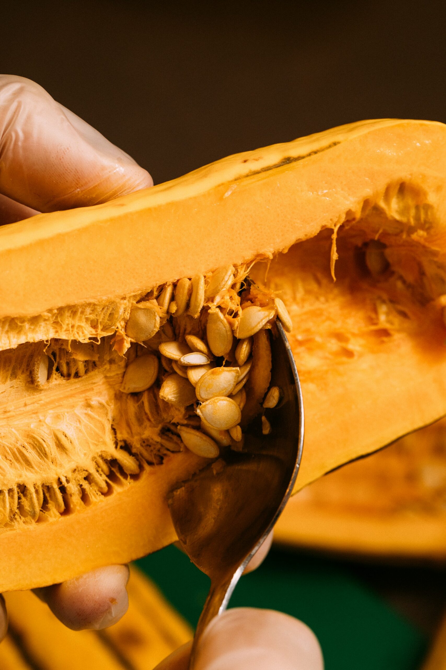 Hands holding half a delicata squash while a spoon scoops out its seeds and stringy pulp