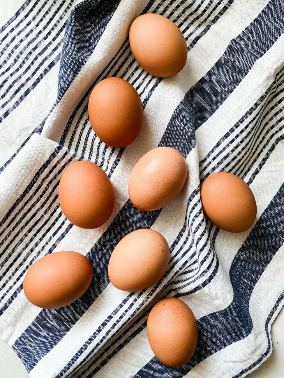 Eight clean brown eggs lying on a blue and white striped cloth